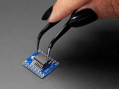 SMT Breakout PCB for SOIC-16 or TSSOP-16 - 3 Pack! - A pair of tweezers holding a microchip hovers over the SMT Breakout PCB for SOIC-16 or TSSOP-16.