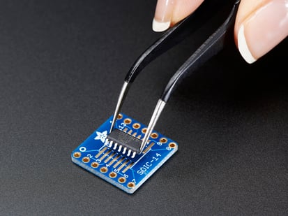SMT Breakout PCB for SOIC-14 or TSSOP-14 - 6 Pack! - A pair of tweezers holding a microchip hovers over the SMT Breakout PCB for SOIC-14 or TSSOP-14.