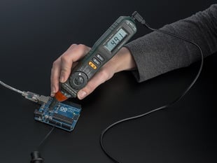 White hand holding a Autoranging Digital Multimeter Pen against an Arduino. Pen reads 4.91.