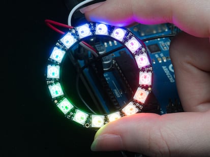 NeoPixel Ring - 16 x 5050 RGB LED with Integrated Drivers - Hand holding NeoPixel Ring with 16 x 5050 RGB LED, lit up rainbow