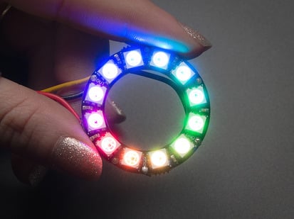 NeoPixel Ring - 12 x 5050 RGB LED with Integrated Drivers - Hand holding NeoPixel Ring with 12  x 5050 RGB LED, lit up rainbow
