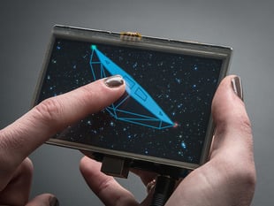 Gray polished white hand holding a Gameduino 2 with 4.3" 480x272 Display and Touchscreen. 