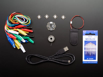Gemma M0 Starter Pack - Kit contents shot with circular microcontroller with copper pads, needles, coin cell battery holder, sewable LEDs, micro USB to USB-A cable, alligator clips, and conductive sewing thread.