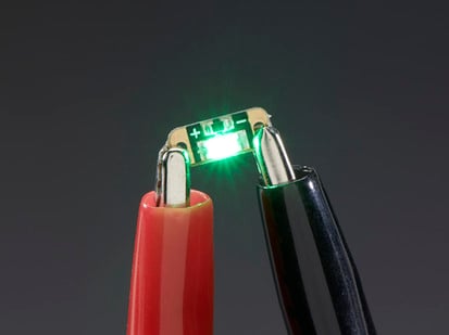 Adafruit LED Sequins - Emerald Green - Pack of 5 - Single LED sequin PCB attached to two alligator clips, glowing green