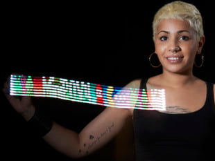 Woman waving MiniPOV kit, with long-capture image showing "MiniPOV4!" in colorful lights.