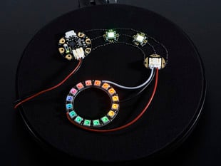 Angled shot of assembled Flora Sewable 3-Pin JST Wiring Adapter connected to glowing LED PCBs and a NeoPixel ring.