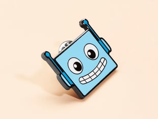 Angled shot of blue enamel pin resembling a friendly robot.