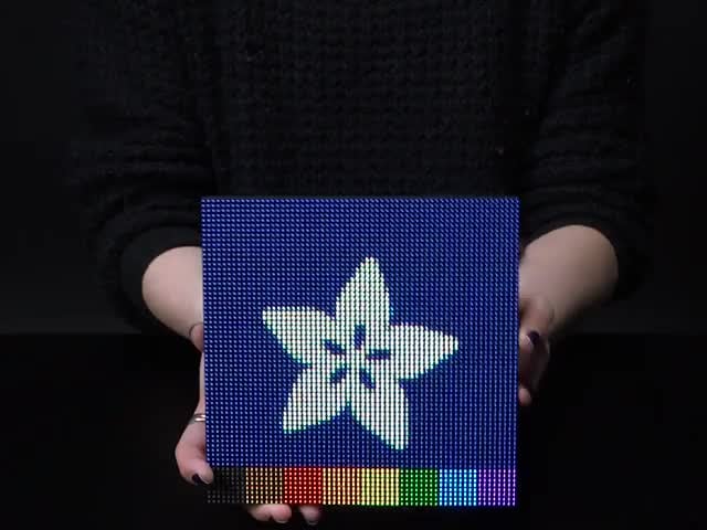 64x64 RGB LED Matrix - 2.5mm Pitch - 1/32 Scan - 1/32 Scan - Video of two hands flipping over a powered on 64x64 RGB LED Matrix. The matrix display has a falling colored sand effect. 