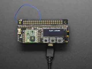 A rectangular microcontroller with OLED screen. A blue-manicured index finger presses buttons below the OLED screen, triggering different texts.