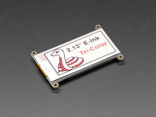 Angled shot of a white, rectangle-shaped electronic ink display breakout with four mounting holes. The display features a friendly python and text: "2.13" E-Ink Tri-Color"