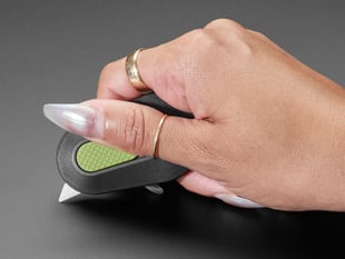 Manicured hand holding pocket cutter with blade extended.