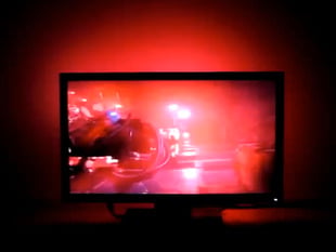 Large flatscreen TV with red-tinted scene and red LEDs lighting wall behind it.