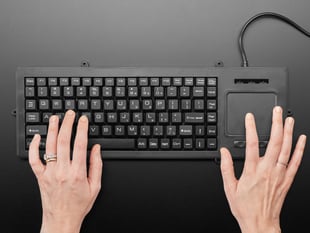 Top view of two white hands typing on full-size keyboard with trackpad.