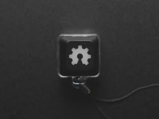 A Black woman's finger presses a keyswitch keychain. A green LED shines beneath an open source hardware logo keycap.