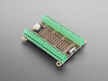 Adafruit Terminal PiCowbell for Pico - Reset Button & STEMMA QT - Angled shot of rectangular prototyping PCB lined with green terminal blocks and mounting holes.