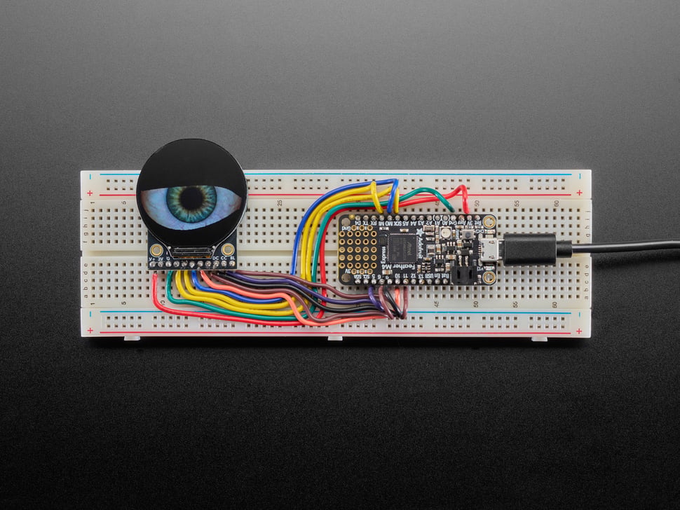 Image of a round TFT display assembled onto a breadboard with a microcontroller. The TFT shows a blinking eyeball animation.