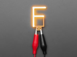 Overhead shot of LED filament in shape of letter "F" lit up with alligator clips.