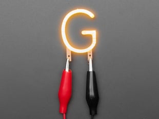 Overhead shot of LED filament in shape of letter "G" lit up with alligator clips.