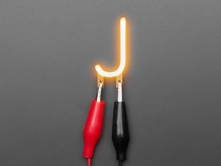 Overhead shot of LED filament in shape of letter "J" lit up with alligator clips.