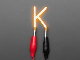Overhead shot of LED filament in shape of letter "K" lit up with alligator clips.