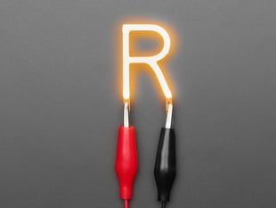 Overhead shot of LED filament in shape of letter "R" lit up with alligator clips.