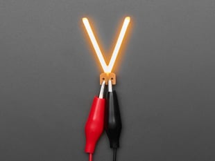 Overhead shot of LED filament in shape of letter "V" lit up with alligator clips.