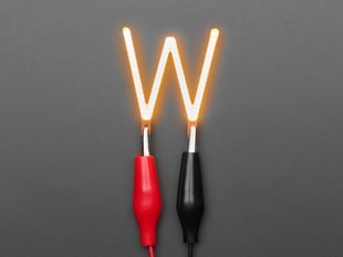 Overhead shot of LED filament in shape of letter "W" lit up with alligator clips.