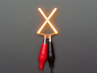 Overhead shot of LED filament in shape of letter "X" lit up with alligator clips.
