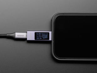 Angled shot of smart phone plugged into OLED analyzer which displays power measurements.