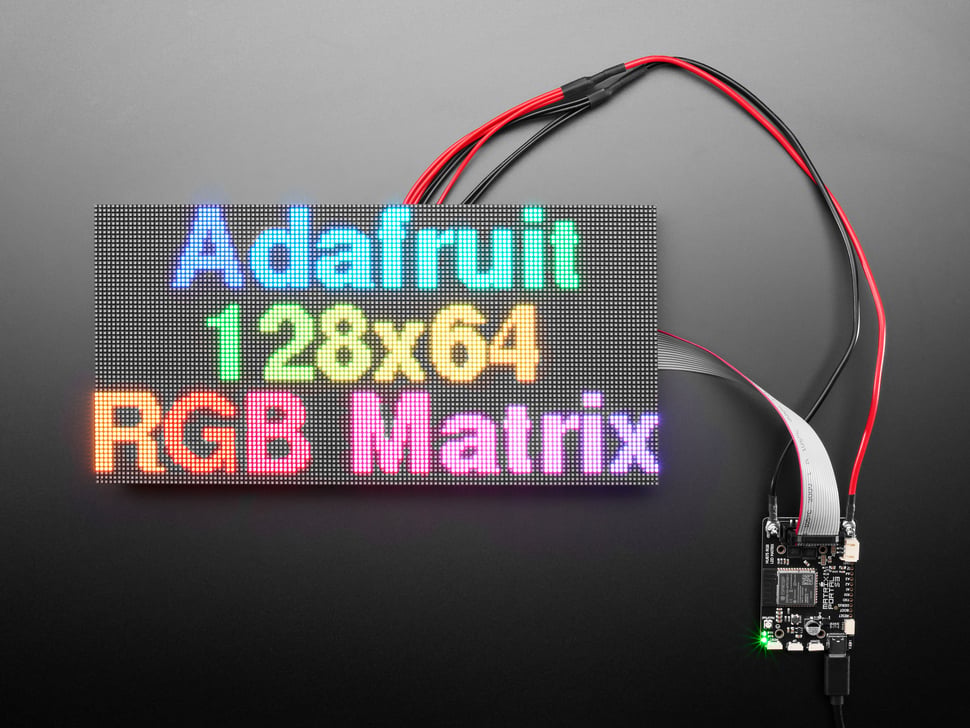 LED matrix panel wired up and displaying "Adafruit 128x64 RGB matrix" in rainbow colors.
