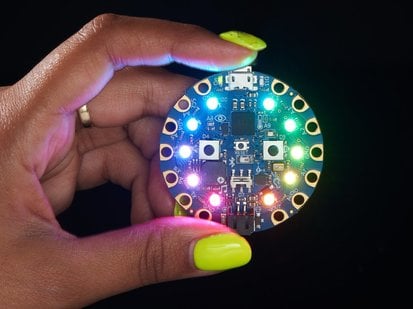 Circuit Playground Bluefruit - Bluetooth® LowEnergy - GH STUDEN - Yellow polished hand holding a rainbow-glowing circuit playground